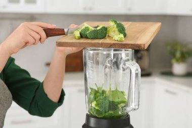 Mutfakta smoothie için malzemelerle karıştırıcıya brokoli ekleyen kadın, yakın plan.