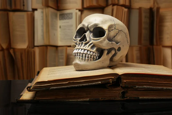 Human skull and old books on mirror table. Space for text