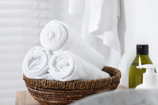 Wicker bowl with rolled bath towels on wooden table indoors
