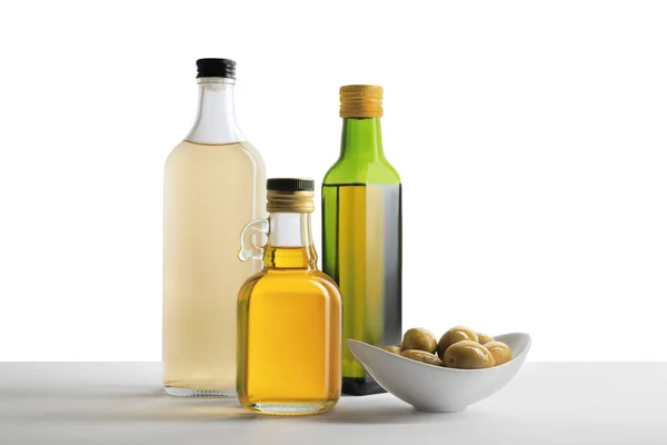 Bottles of different cooking oils and olives on white background