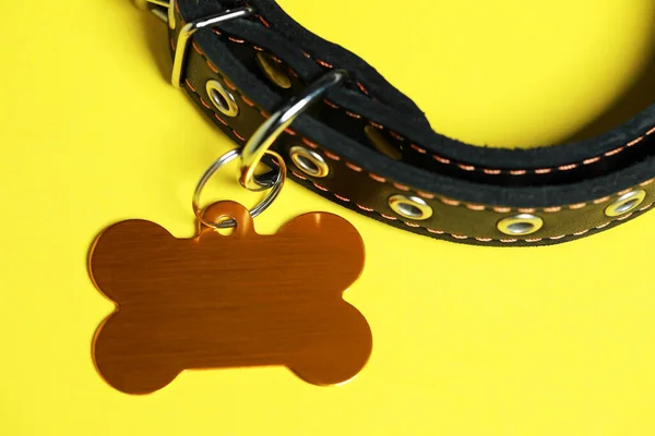 Black leather dog collar with golden tag in shape of bone on yellow background, closeup. Space for text