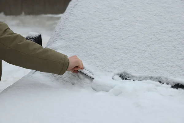 Woman cleaning car wiper blade covered with snow outdoors, closeup