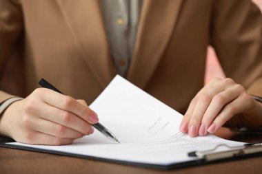 Woman signing documents at wooden table in office, closeup clipart