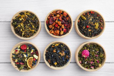 Beyaz ahşap masadaki kaselerde farklı türde kuru bitkisel çay.