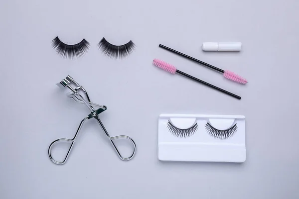 Flat lay composition with fake eyelashes, brushes and tool on light grey background