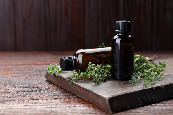 Bottles of thyme essential oil and fresh plant on wooden table, space for text