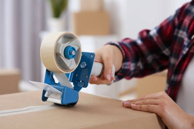 Kadın kutuya yapışkan bant yapıştırıyor. Kapalı mekanda, yakın plan.