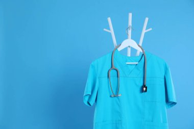 Turkuaz tıp üniforması ve steteskop açık mavi arka planda asılı duruyor. Metin için boşluk