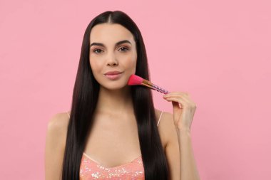 Güzel bir kadın pembe arka planda fırçayla makyaj yapıyor. Metin için boşluk
