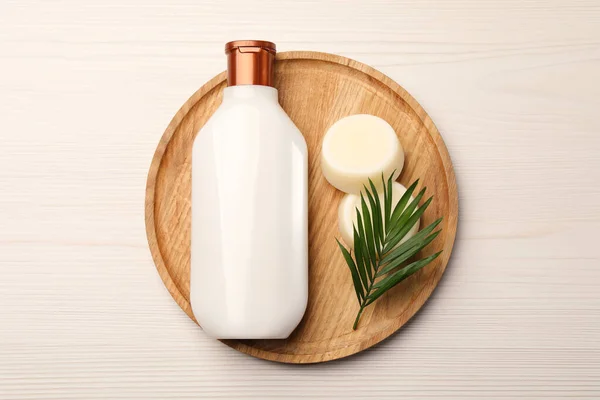 Shampoo bottle, solid shampoo bars and green leaf on white wooden table, top view