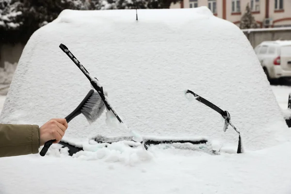 Woman cleaning car wiper blade from snow with brush outdoors, closeup