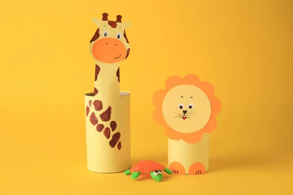 Toy giraffe and lion made from toilet paper hubs with plasticine turtle on yellow background. Children\'s handmade ideas