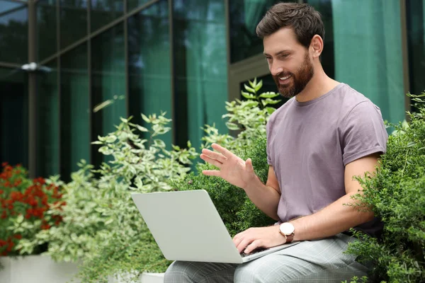 Handsome man with laptop near beautiful plants on city street