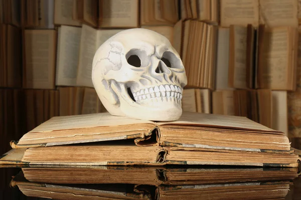 Human skull and old books on mirror table
