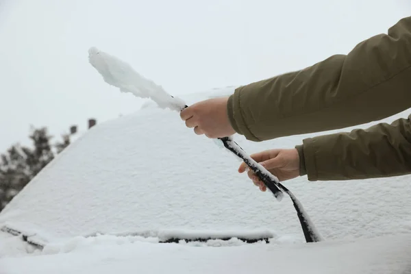 Woman cleaning car wiper blade covered with snow outdoors, closeup