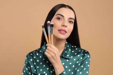 Açık kahverengi arka planda farklı makyaj fırçaları olan güzel bir kadın.
