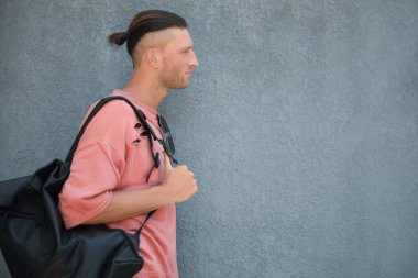 Gri duvarın yanında şık güneş gözlüklü ve çantalı yakışıklı genç adam, mesaj için yer var.