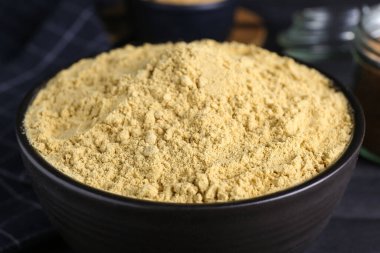 Bir kase aromatik hardal tozu siyah ahşap masada, yakın plan.