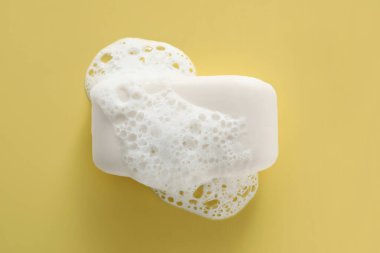 Sarı arka planda kabarık köpüklü sabun çubuğu, üst görünüm