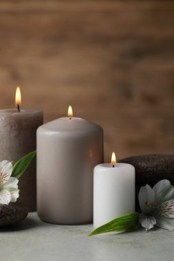 Yanan mumlarla, spa taşlarıyla ve açık gri masadaki çiçeklerle güzel bir kompozisyon.