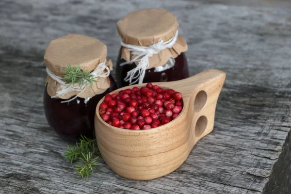 Tasty lingonberry jam in jars and cup with red berries on wooden table