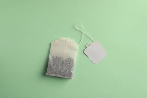 Paper tea bag with tag on light green background, top view