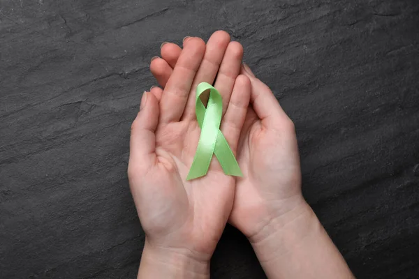 World Mental Health Day. Woman holding green ribbon on black background, top view