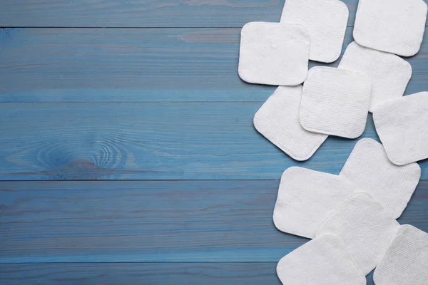 Many clean cotton pads on light blue wooden table, flat lay. Space for text