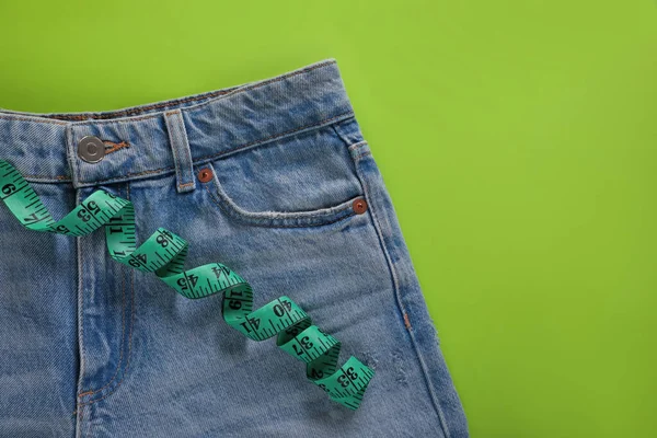 Jeans and measuring tape on light green background, top view with space for text. Weight loss concept