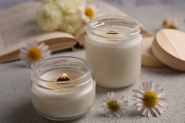 Burning scented candles and chamomile flowers on light gray textured table, closeup