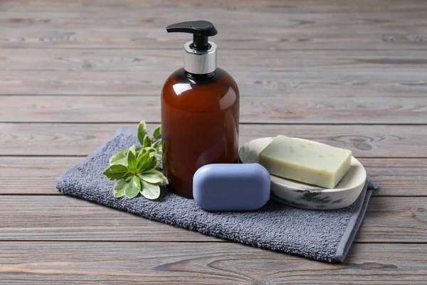 Soap bars, dispenser and terry towel on wooden table,