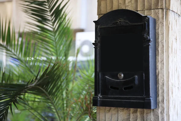 Black metal letter box on beige column outdoors, space for text
