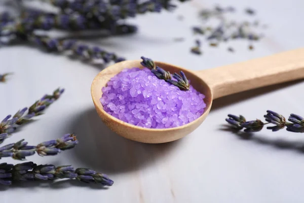 Spoon with purple sea salt and lavender on wooden table, closeup