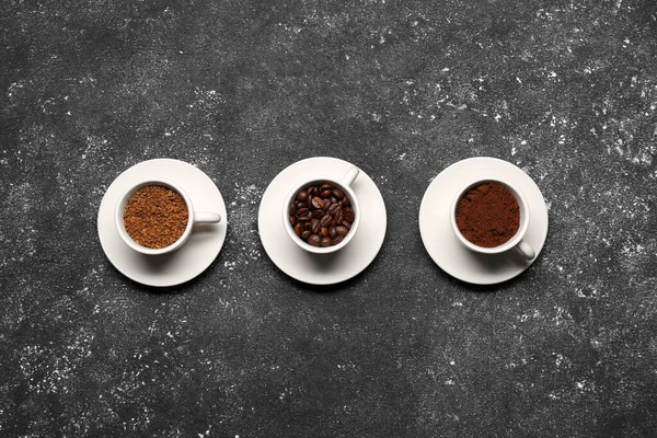 Cups with different types of coffee on dark grey table, flat lay