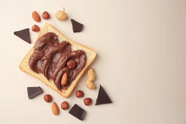 Tasty toast with chocolate paste and nuts on beige background, flat lay. Space for text