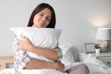 Yatakta yastığa sarılan güzel bir genç kadın.