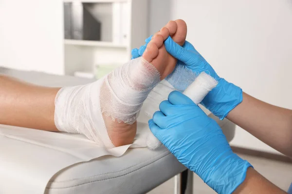 Doctor applying bandage onto patient\'s foot in hospital, closeup