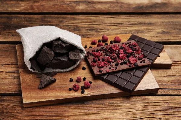 Board and different chocolate bars with freeze dried fruits on wooden table