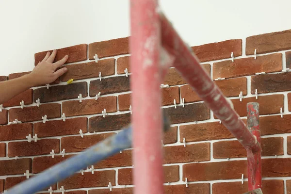 Profesyonel müteahhit duvara dekoratif tuğla yapıştırıyor, yakın plan. Döşeme kurulum süreci