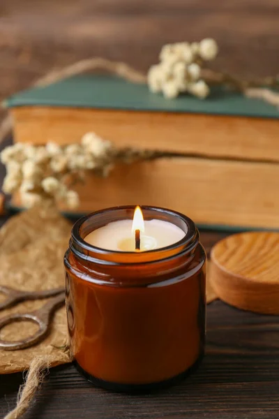 Burning scented candle, book and flowers on wooden table