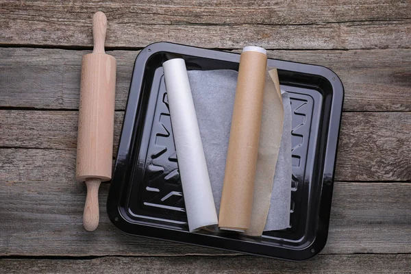 Rolls of parchment paper in baking pan and rolling pin on wooden table, flat lay
