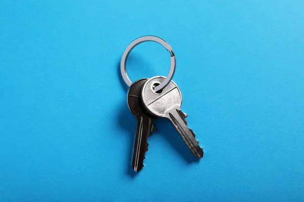 House keys on light blue background, top view. Real estate agent services
