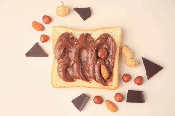 Tasty toast with chocolate paste and nuts on beige background, flat lay