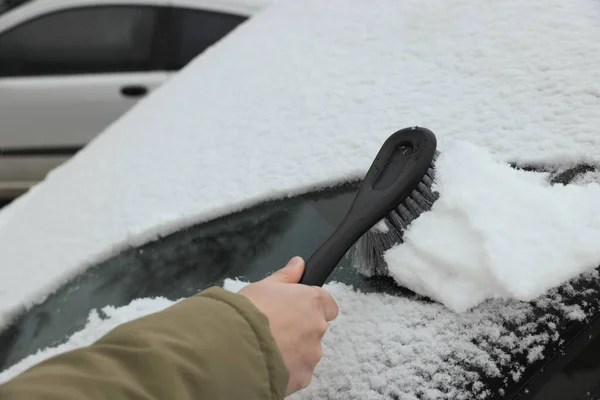 Woman cleaning car windshield from snow with brush outdoors, closeup