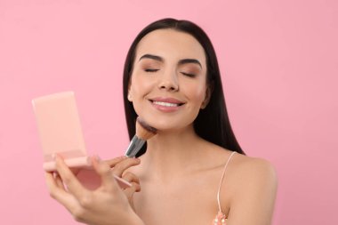 Kozmetik cep aynalı güzel bir kadın pembe arka plana makyaj yapıyor.