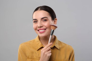 Açık gri arka planda makyaj fırçası olan mutlu kadın.