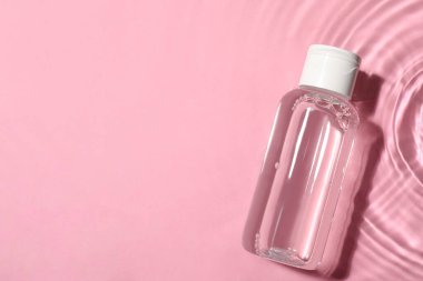 Pembe arka planda ıslak bir şişe mikiler suyu, üst manzara. Metin için boşluk