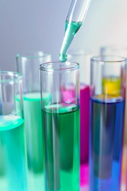 Gri arkaplanda pipetten test tüpüne sıvı damlatılıyor, yakın plan.