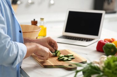 Adam mutfakta dizüstü bilgisayarla yemek kursunu izlerken yemek hazırlıyor.