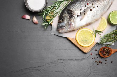 Düz kompozisyon, taze çiğ dorado balığı ve malzemeleri siyah masa üzerinde, metin için boşluk.